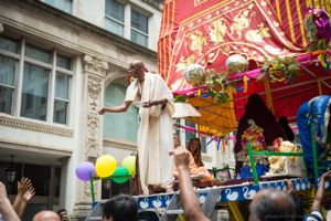 A festival participant holds a hand out over the crowd from where they stand on a cart