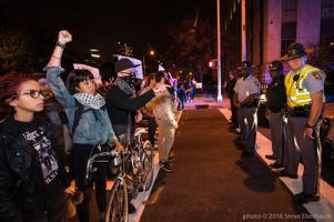Protesters raise their fist in the air and point their fingers as they stand in front of a police blockade