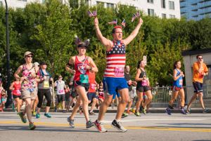 A man wearing an American Flag tank top runs by waving American Flags