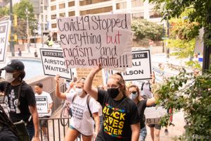A protester holds up a sign reading 'COVID-19 Stopped Everything but Racism and Police Brutality'