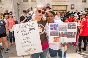 Protesters stand toegther, holding up signs that wishes to 'End White Supremacy!' and one with lots of pictures on it