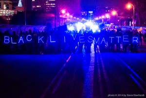 Protesters march over a bridge holding a glowing Black Lives Matter sign