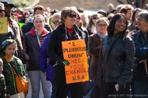 A protester holds a sign reading '""E Pluribus Unum"" Check your Change, U.S.A'