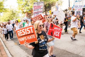A protester marches down the street holding signs that read 'We Will Resist Trump's Hate' and 'Abolish Ice'