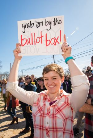 A woman holds up a sign reading 'Grab 'em by the Ballot box!'