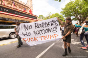 Protesters hold a sign, "No Borders No Nations Fuck Trump"