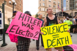 Protesters holding signs, "Hitler was elected 2" and "Silence = death".