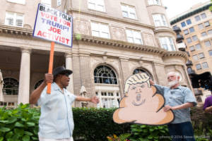 Protesters hold signs, "Black folk vote for Trump! Joe Activist" and sign shaped like feces with Trump's face.