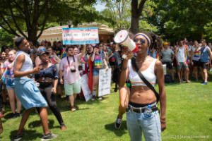 Protester speaks on a megaphone while others dancea and hold signs