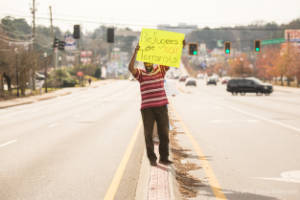 A man standing in the middle of a street holds a sign that reads "Refugees are not terrorists"