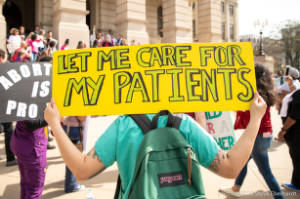 Protester in scrubs with sign, "Let me care for my patients"