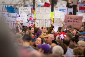 A crowd of protesters hold signs, including "Guns are stupid"