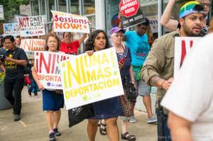 Protesters walk with signs, including "Ni una mas deportacion!"