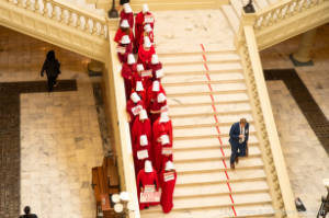 Protesters dressed as characters from Handmaiden's Tale on stairs in two columns