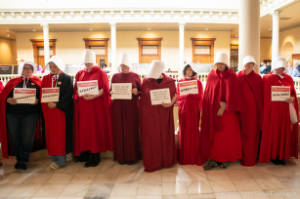 Protesters dressed as characters from Handmaiden's Tale hold signs, including "HB481 will responsible for killing women & girls"