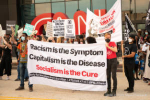 Protesters hold a banner that reads, "Racism is the Sympton. Capitalism is the Disease. Socialism is the Cure."