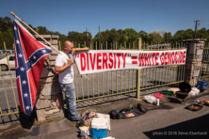 A man hangs a banner that reads, "Diversity equals white genocide"