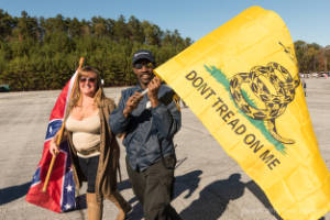 A man carrying a flag that reads, "Don't tread on men" walks next to a woman carrying a Confederate flag