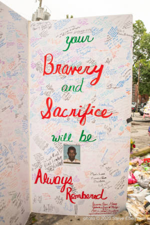 A large card that reads, "Your bravery and sacrifice will be always remembered" sits in a parking lot