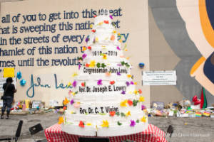 A large cake with the names of John Lewis, Joseph E. Lowry, and C.T. Vivian sits in a parking lot