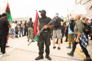 A protester standing in the street holds a shotgun