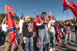 A man holding a Bible stands next to people holding Confederate flags