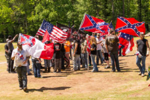 A group of people hold Confederate flags in a grassy field