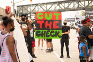 Protesters hold a sign that reads, "Cut the check"