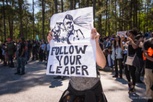A protester holds a sign that reads, "Follow your leader"