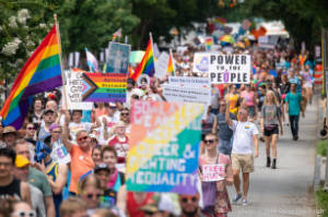 Protesters march with signs, "Marsha & Sylvia & Storme & Craig & Fred & Us." and "Power to the People"