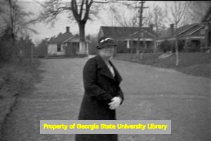 Older woman dressed in black walking in a neighborhood, Atlanta, Georgia, circa late 1930s or early 1940s