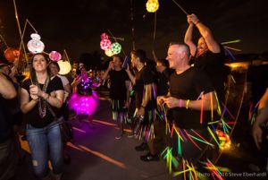 A group of people covered in glowsticks watch as lanterns go by