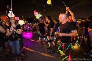 A group of people covered in glowsticks watch as lanterns go by