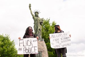 Protesters stand next to a replica Statue of Liberty holding signs