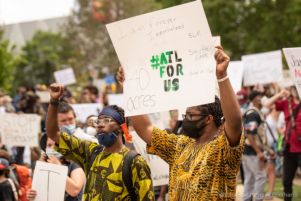 A protester holds up a sign reading '#ATLForUs, 40 Acres, I Am Forever Immortalized, BLM, Say Their Name, United We Stand'