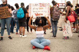 A protester sits holding sign 'I am tired of my skin being seen as a weapon'