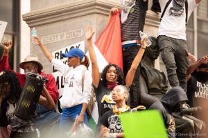 Protesters stand at the base of the Henry Grady statue holding their hands in the air