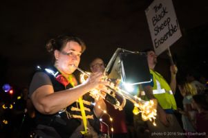 A woman plays a trumpet wrapped in lights