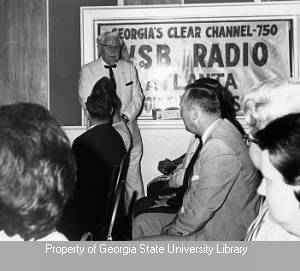 Harland Sanders addressing an audience in front of a WSB banner