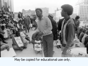 Protest organizer addressing Atlanta Garbage Strike protestors on steps and sidewalk of Atlanta City Hall, downtown Atlanta, Georgia, March 31, 1970. One in a series of negatives labeled "Strike."