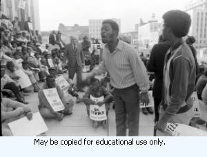 Protest organizer addressing Atlanta Garbage Strike protestors on steps and sidewalk of Atlanta City Hall, downtown Atlanta, Georgia, March 31, 1970. One in a series of negatives labeled "Strike."