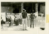 Protester speaks into microphone in front of banners, "W.VA SCEF Dema[nds] Decent Hous[ing for] Working [Peop]le!"