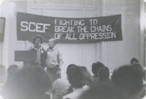 Two people speak a microphone by podium