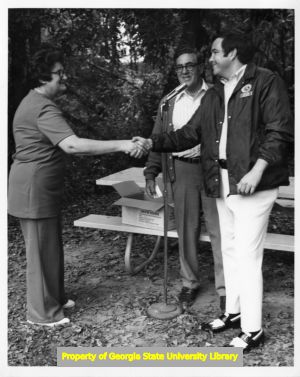 Herb Green speaking into a microphone with two others.