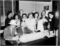 Office staff standing around a desk that has a large aerial bomb on the edge. Calendar on the wall open to October. Photo commissioned by the DeKalb New Era.