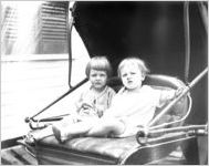 Two infants sitting on a buggy seat.