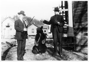 Men posing with a gun and a chained bear, circa 1920s