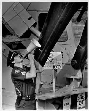 A police officer calls for Mary Newson to come down from a crane that she chained herself to, undated