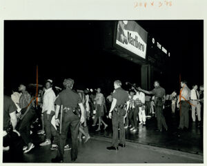 Officers attempt to control a crowd that has gathered at the scene of a shooting, July 28, 1985