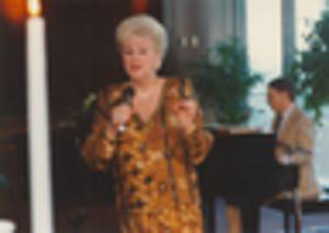 Woman singing, with man accompanying on piano in background